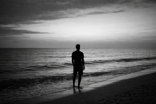 Person standing alone by the ocean in black and white, looking out into the distance, reflecting patience and acceptance of what is not yet here